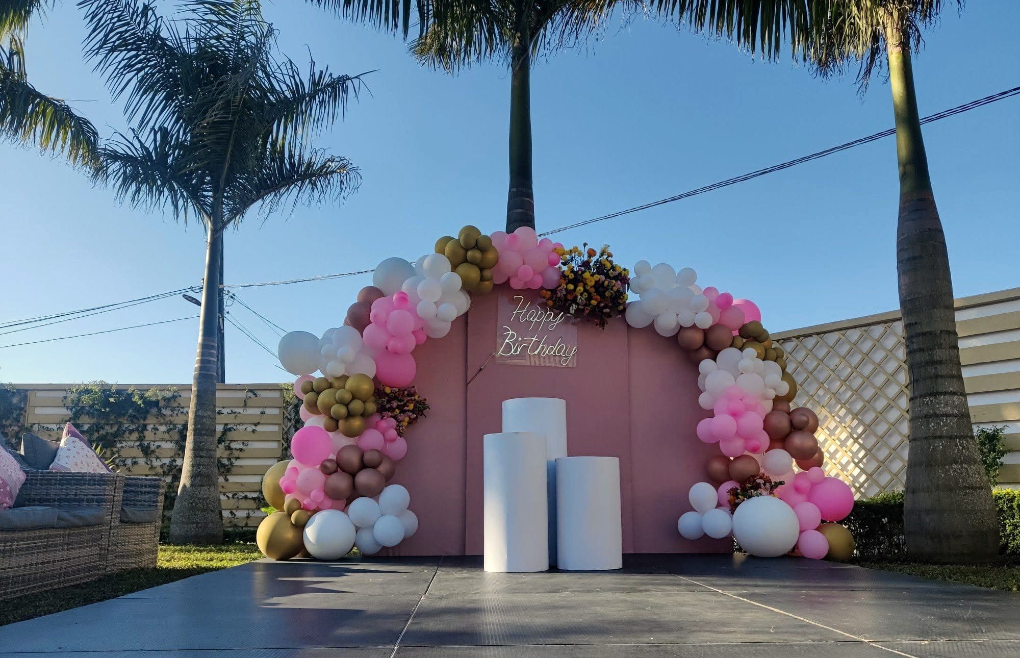 Arche de ballons roses et dorés sous les palmiers pour un anniversaire